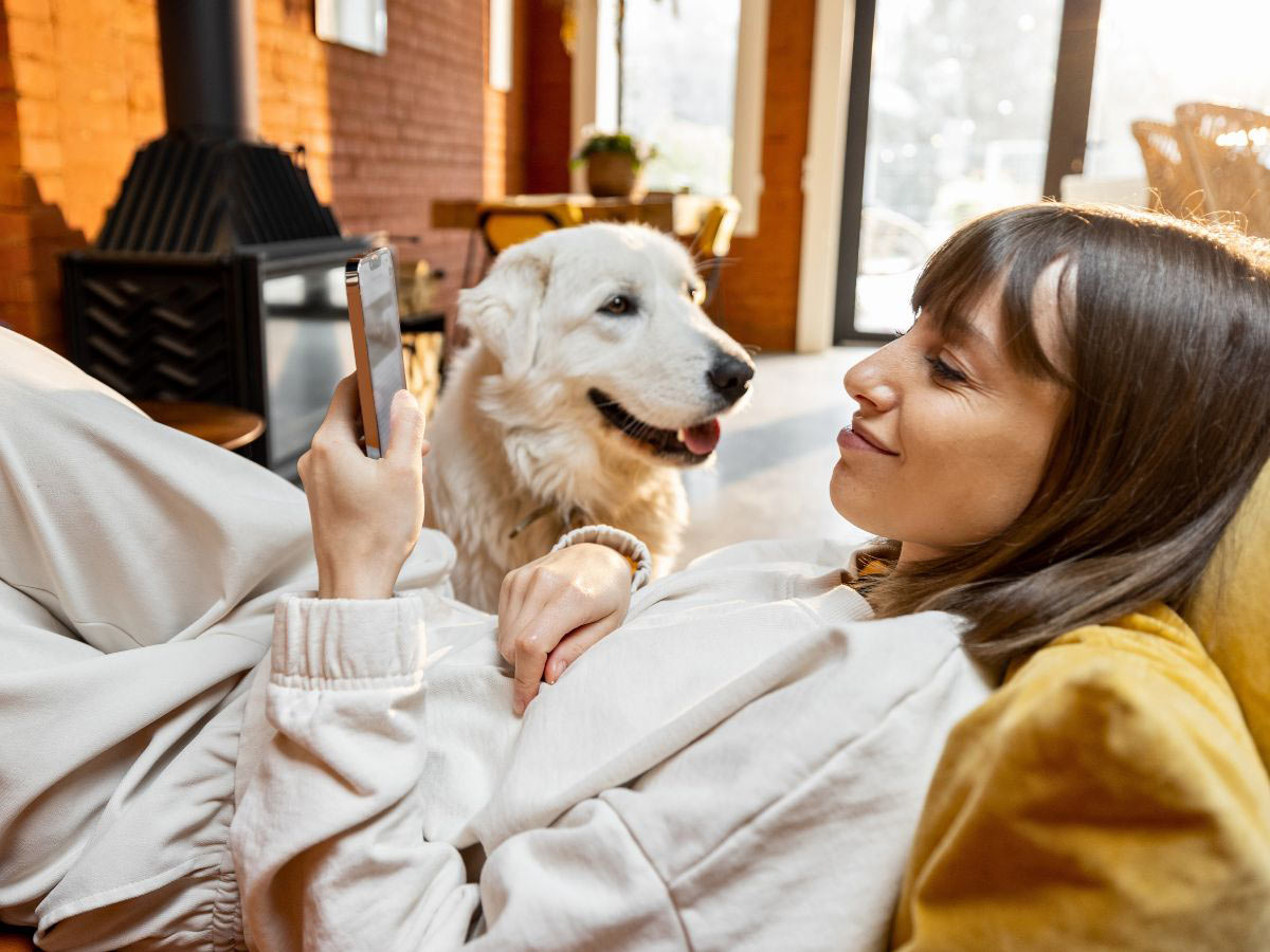smiling woman using her phone next to her happy dog